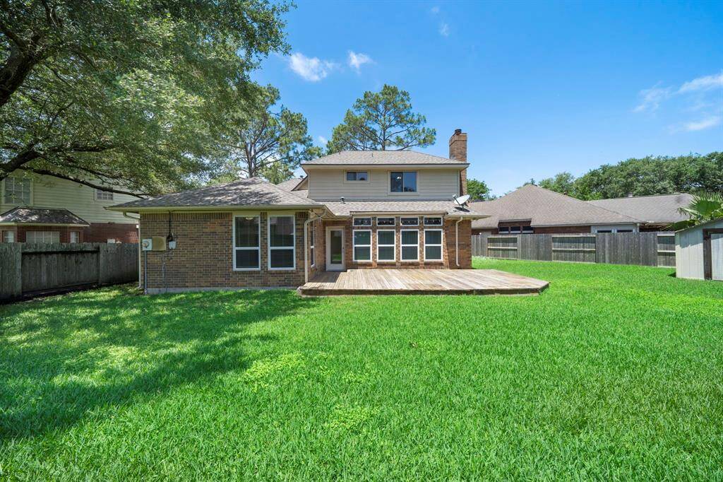 This home features a wooden deck perfect for outdoor gatherings and is surrounded by a well-maintained lawn and mature trees.