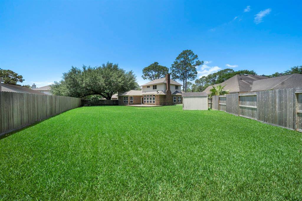 Spacious backyard with lush green lawn, privacy fencing, and mature trees, ideal for outdoor activities and gatherings.
