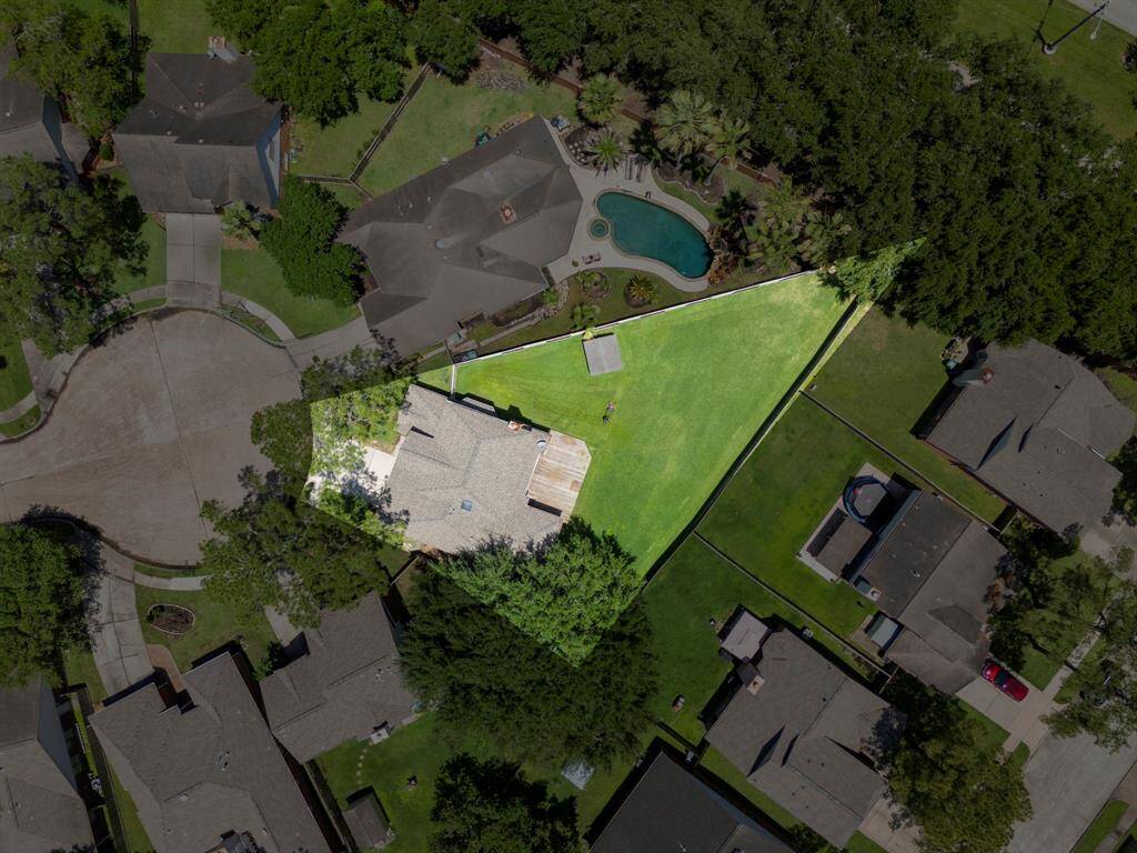 This aerial view shows a home with a unique triangular lot in a quiet cul-de-sac. The property features a large, well-maintained lawn, ample outdoor space, and is surrounded by mature trees.