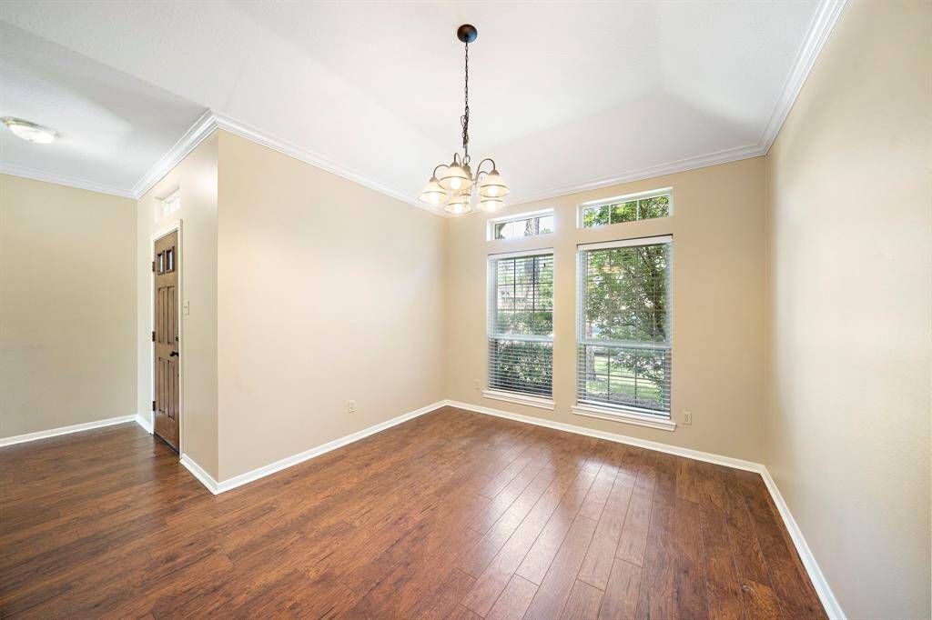 This bright, inviting room features warm wood flooring and large windows for natural light. The neutral walls and crown molding create a clean, modern look, perfect for a dining, living area, or office space.