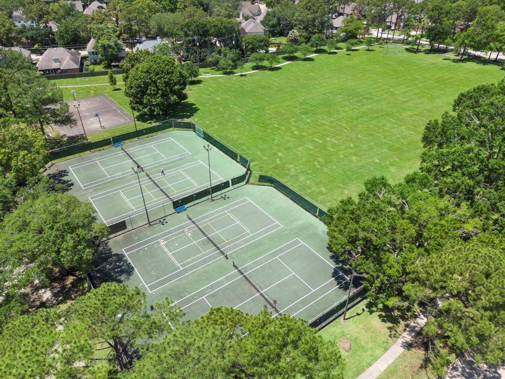 This aerial photo showcases a neighborhood with pickleball and tennis courts and a large open grassy area.