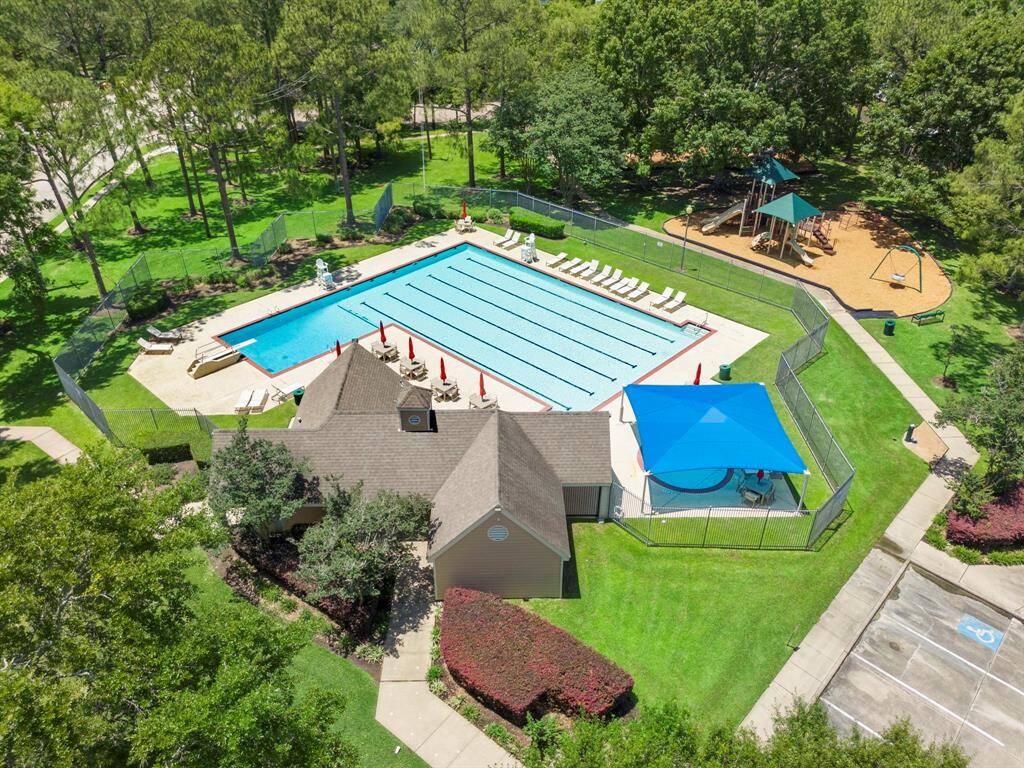This photo showcases a community recreational area featuring a large swimming pool, a clubhouse, and a playground, all surrounded by lush greenery.