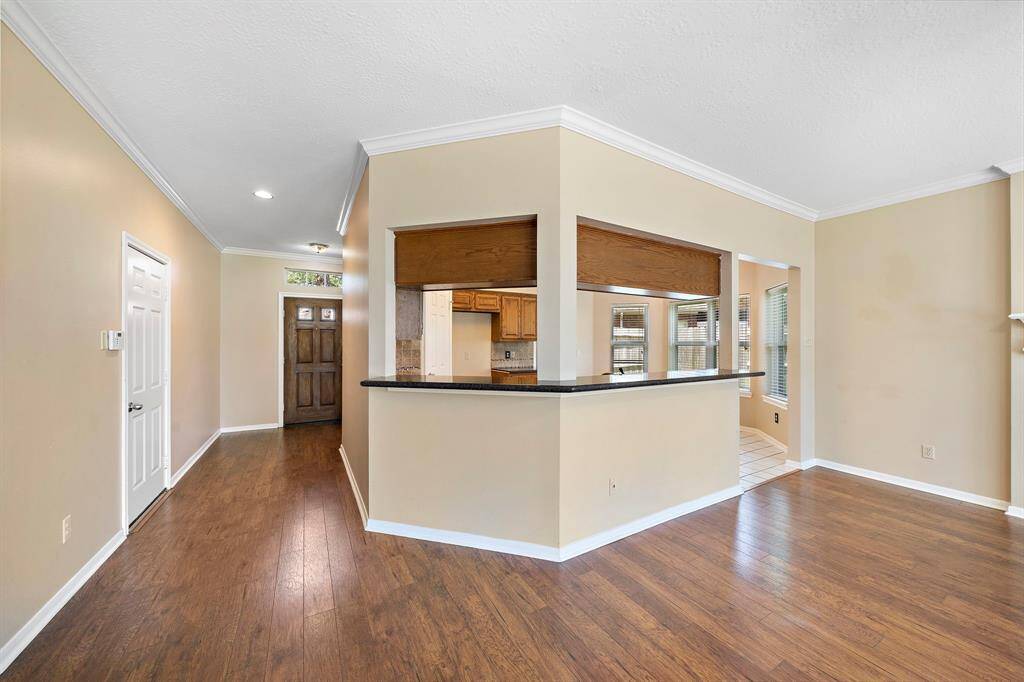 Bright and inviting entryway with wood flooring and neutral walls, featuring an open kitchen pass-through with a bar counter. Ample natural light from multiple windows, enhancing the spacious feel.