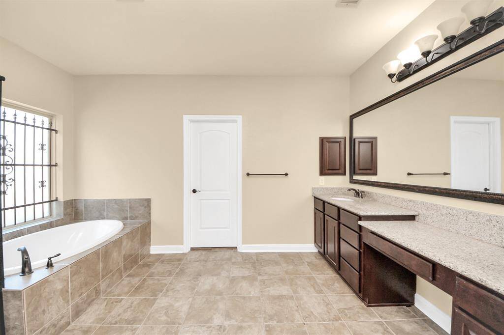 Spacious bathroom with a large soaking tub, elegant tile flooring, and ample counter space. Features a wide mirror, dual sinks, and stylish lighting.