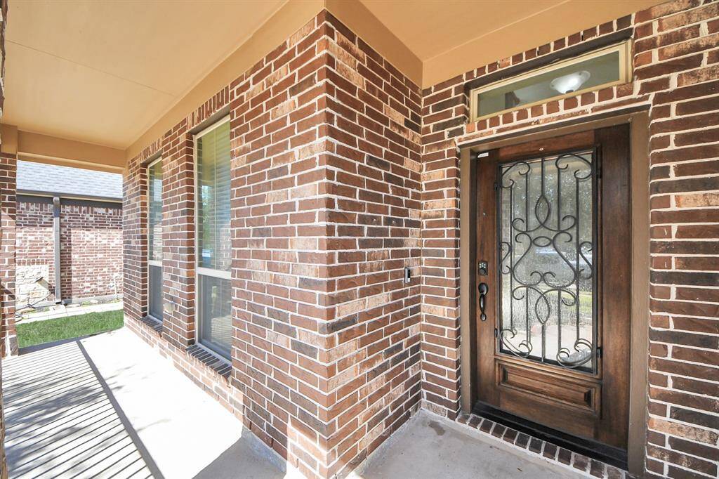 This photo shows a welcoming brick exterior with a covered front porch. The entrance features a decorative wooden door with intricate wrought iron detailing, flanked by large windows for natural light.