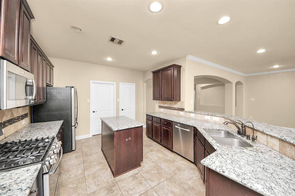 This kitchen features granite countertops, stainless steel appliances, and dark wood cabinets. It includes a central island, dual sinks, and ample lighting, creating a spacious and modern cooking area.