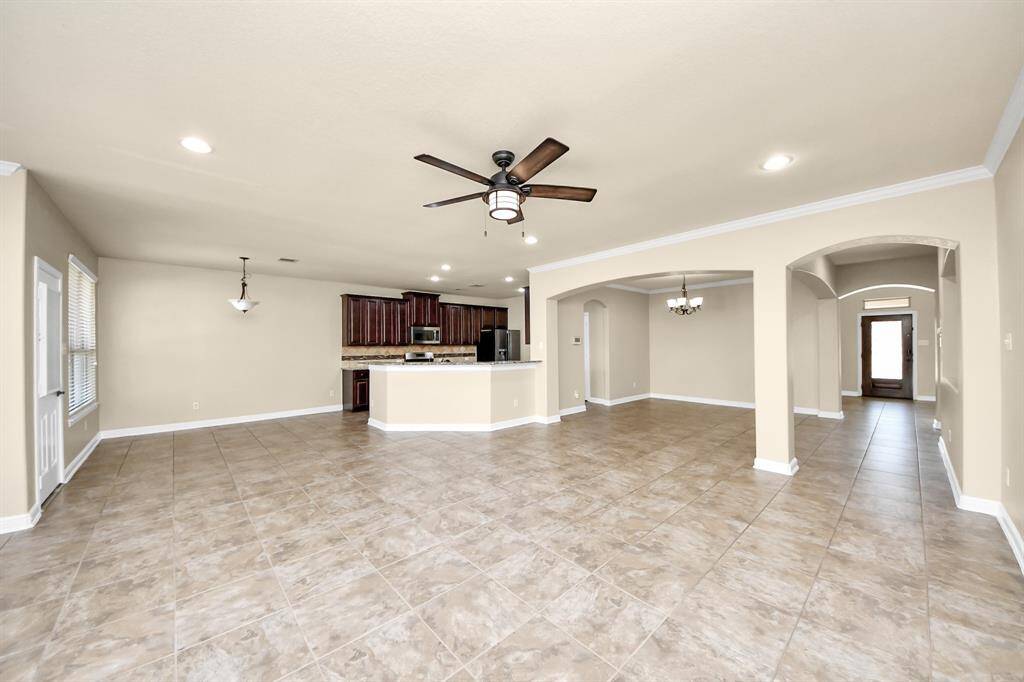 This photo showcases a spacious open-concept living area with tiled floors, a ceiling fan, and recessed lighting. The modern kitchen features dark wood cabinets and stainless steel appliances, with an island for additional counter space. Arched entryways lead to adjacent rooms, enhancing the airy feel.