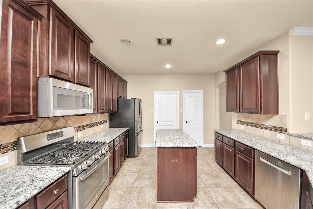 This kitchen features modern stainless steel appliances, granite countertops, and rich dark wood cabinetry. It offers ample storage and workspace, with a spacious layout ideal for cooking and entertaining.