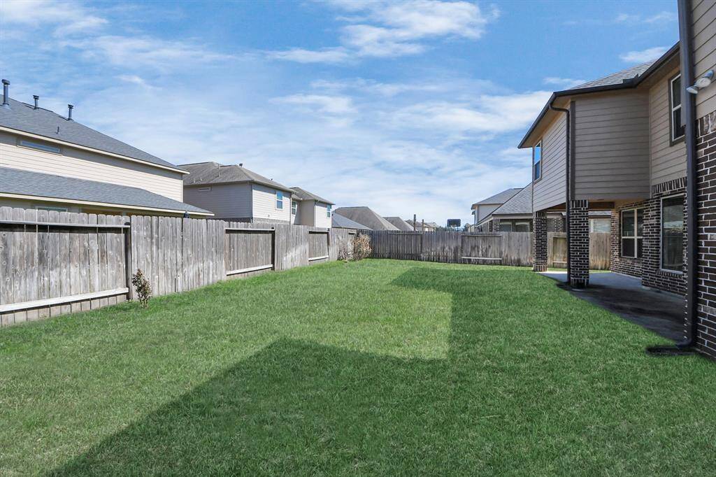 Spacious backyard with a well-maintained lawn, enclosed by a wooden fence, providing privacy. The area features a covered patio adjacent to a two-story home, perfect for outdoor activities and relaxation.