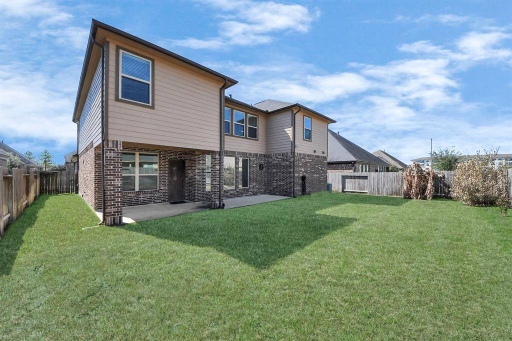 This photo showcases a two-story home with a combination of brick and siding exterior. It features a spacious, well-maintained backyard with a grassy lawn, fenced for privacy. The house has multiple windows, allowing for natural light, and there is a small concrete patio area.