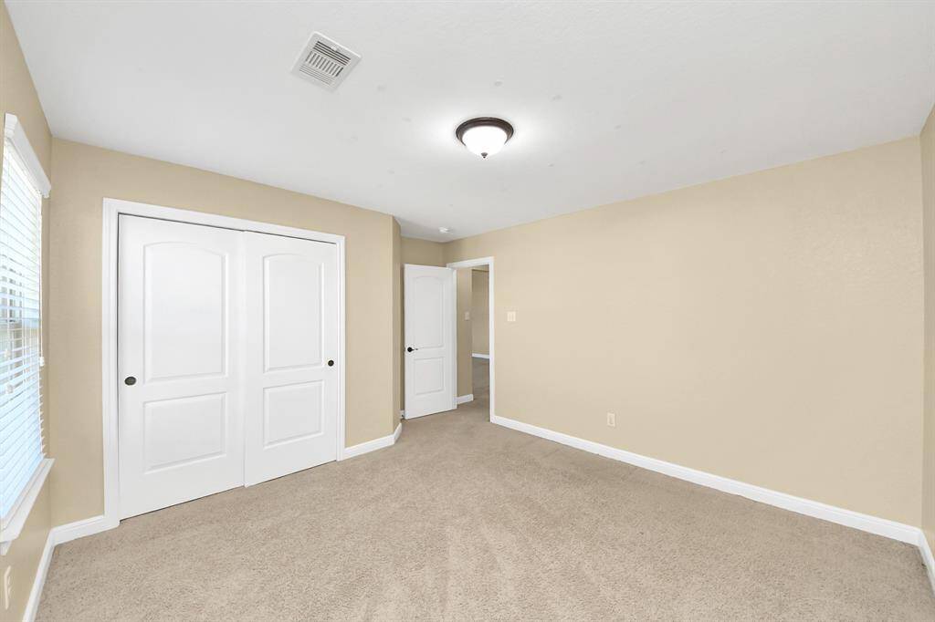 This room is spacious with neutral-colored walls and carpeted flooring. It features a window for natural light, a ceiling light fixture, and a double-door closet. The simple design offers versatility for various uses.