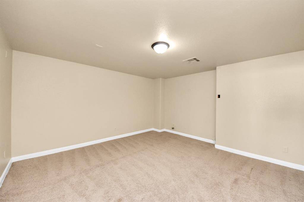 This photo shows a spacious, carpeted room with neutral beige walls, a central ceiling light, and white baseboards. It's ideal for a basement or bonus room.