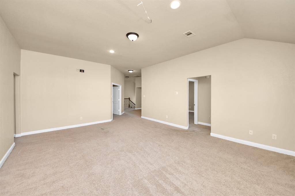 This is a clean, unfurnished room with beige walls and carpet flooring. It features a window for natural light, a ceiling light fixture, and a door leading to another area. Perfect for a bedroom or home office.