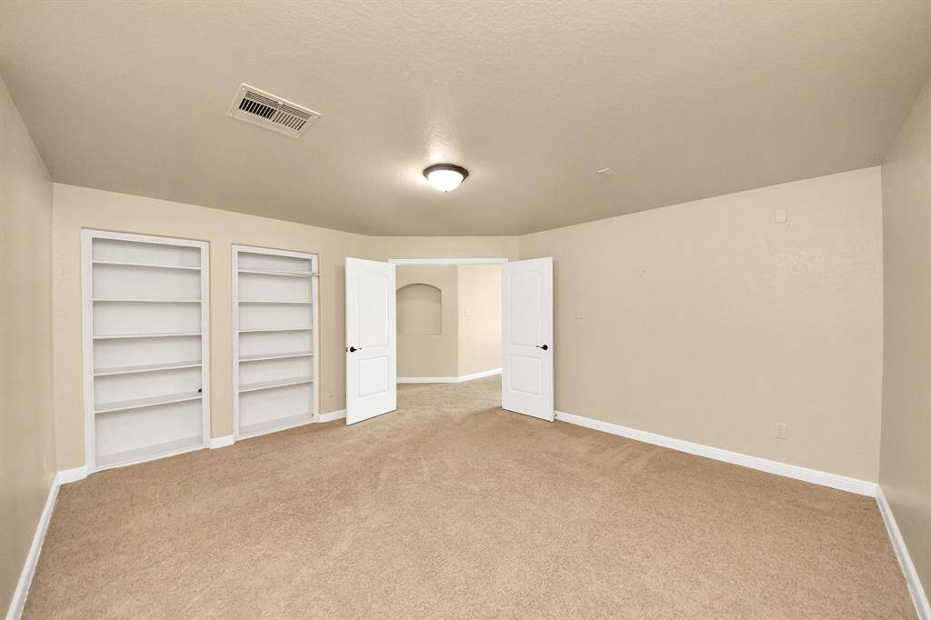This MEDIA  ROOM features neutral walls and carpet, built-in shelving for storage, and a ceiling light fixture. It has double doors leading to another space, offering an open and versatile layout.