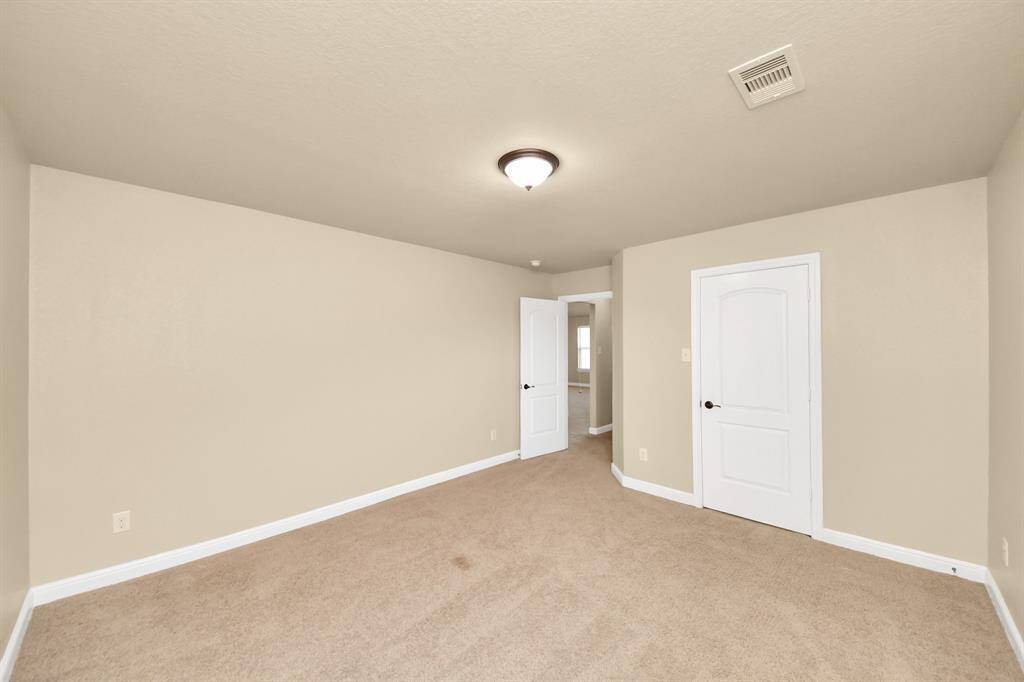 This spacious room features neutral tones with carpet flooring, multiple windows for natural light, and a recessed ceiling with modern lighting. Ideal for a living area or bedroom suite