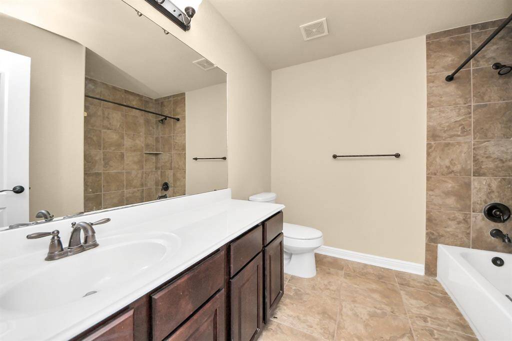 This bathroom features a large mirror above a double-sink vanity with dark wood cabinets. It includes a bathtub with a tiled shower area and neutral tile flooring for a clean, modern look.
