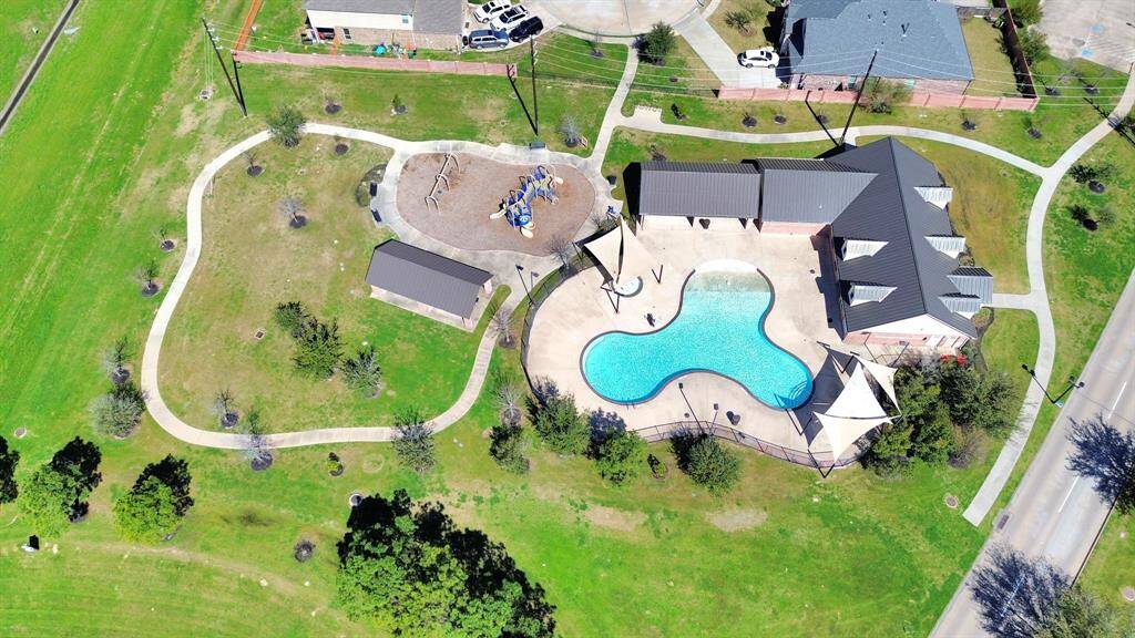 This aerial photo showcases a community area with a uniquely shaped pool, a playground, and green spaces. A modern clubhouse with shaded areas surrounds the pool, making it ideal for family activities and relaxation.