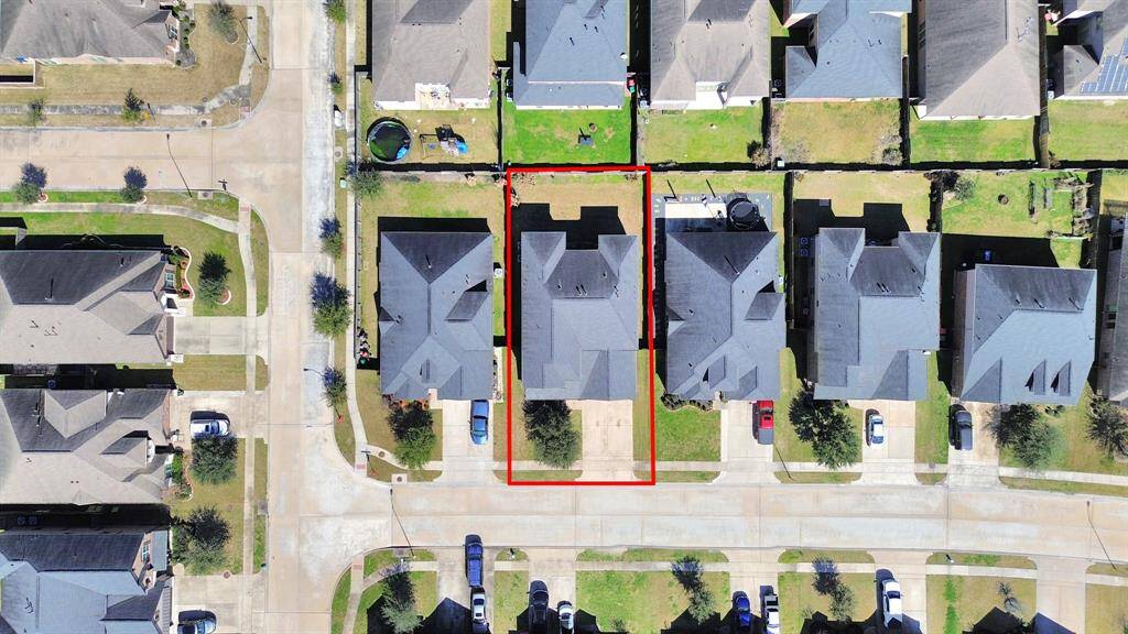 This aerial photo shows a residential neighborhood with the highlighted property featuring a centrally located house on a well-maintained lot. The house has a driveway and backyard, and is situated in a quiet, suburban setting with nearby homes of similar style.