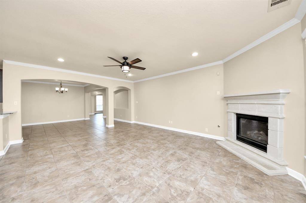 This spacious living area features neutral tones, a tiled floor, and a cozy fireplace. It has a ceiling fan for comfort and opens into a dining space with elegant lighting. Perfect for entertaining or relaxing.