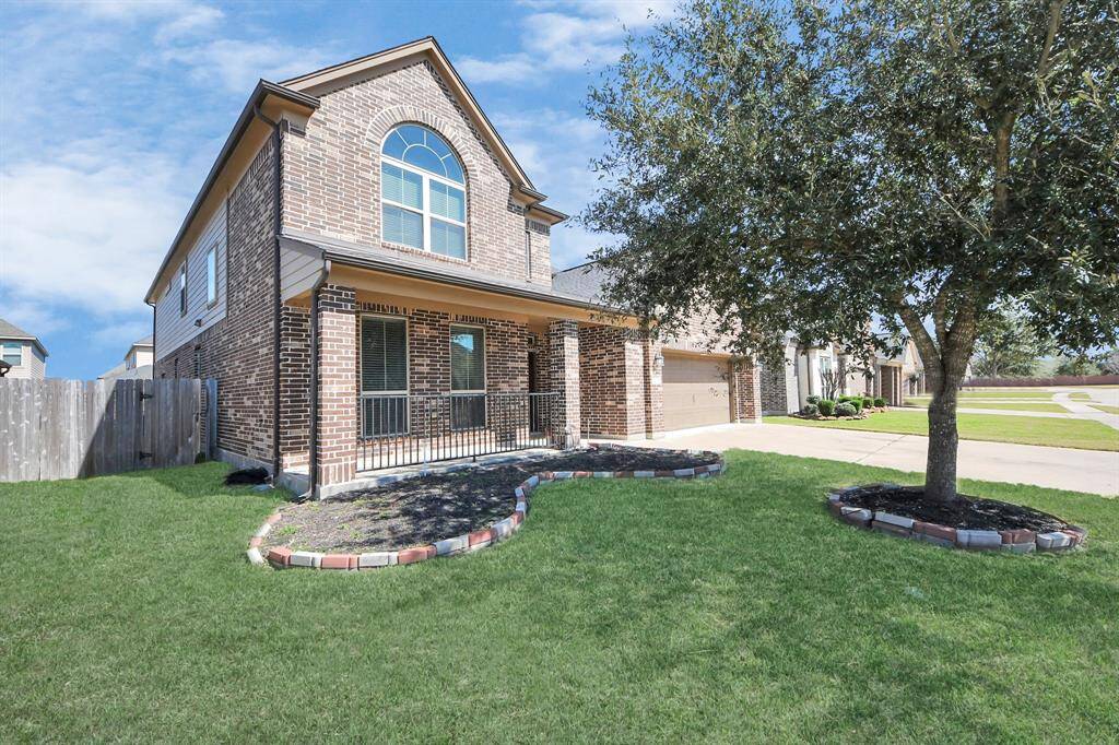 This photo showcases a two-story brick house with a two-car garage. It features a well-maintained front yard with a large tree and is situated on a corner lot with a spacious driveway.