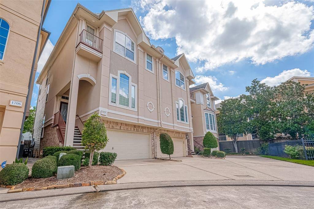 Experience modern living in this elegant multi-story townhouse, featuring a stylish beige facade, large windows, and a two-car garage. Enjoy the inviting entrance with its elevated stairs and beautifully landscaped surroundings with trimmed bushes and small trees.