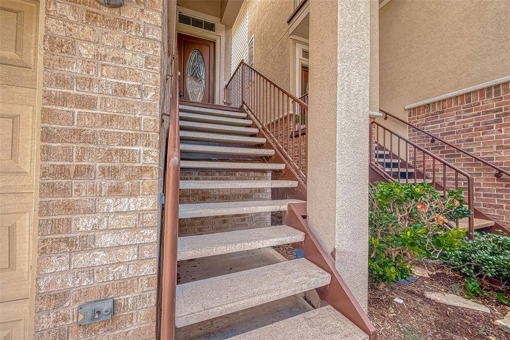 This photo shows an exterior staircase leading to a front door with decorative glass, surrounded by brick and stucco walls. The area is nicely landscaped, offering a welcoming entrance to the home.