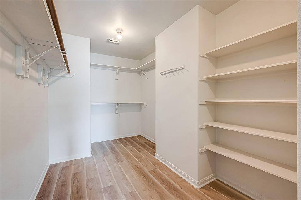 Spacious walk-in master closet with ample shelving and hanging space, featuring light wood flooring and bright, neutral walls for a clean, organized look.