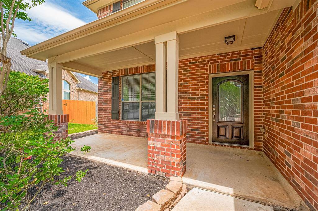 Charming covered porch with brick columns and glass-panel door—warm and welcoming.