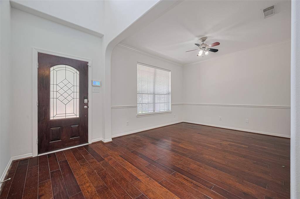 Bright entryway with rich hardwood floors, crown molding, and a striking glass-panel front door for a warm first impression.