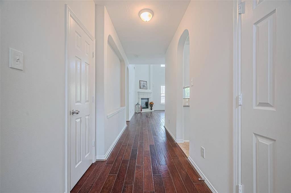 Long hallway with rich wood floors, arched openings, and a view into the bright, open living room.
