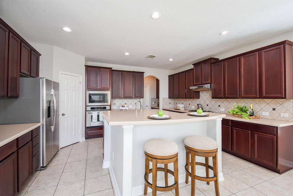 The kitchen pairs rich cabinetry with a complementing backsplash and smooth countertops, creating a harmonious design. A center island with raised bar seating offers casual dining space, while recessed lighting enhances the ambiance.