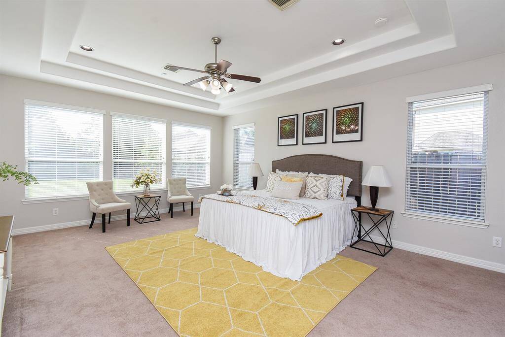 Generously proportioned and carpeted for comfort, the primary suite has expansive windows, a tray ceiling, and a ceiling fan. Double doors lead into a private en suite bath for added luxury.