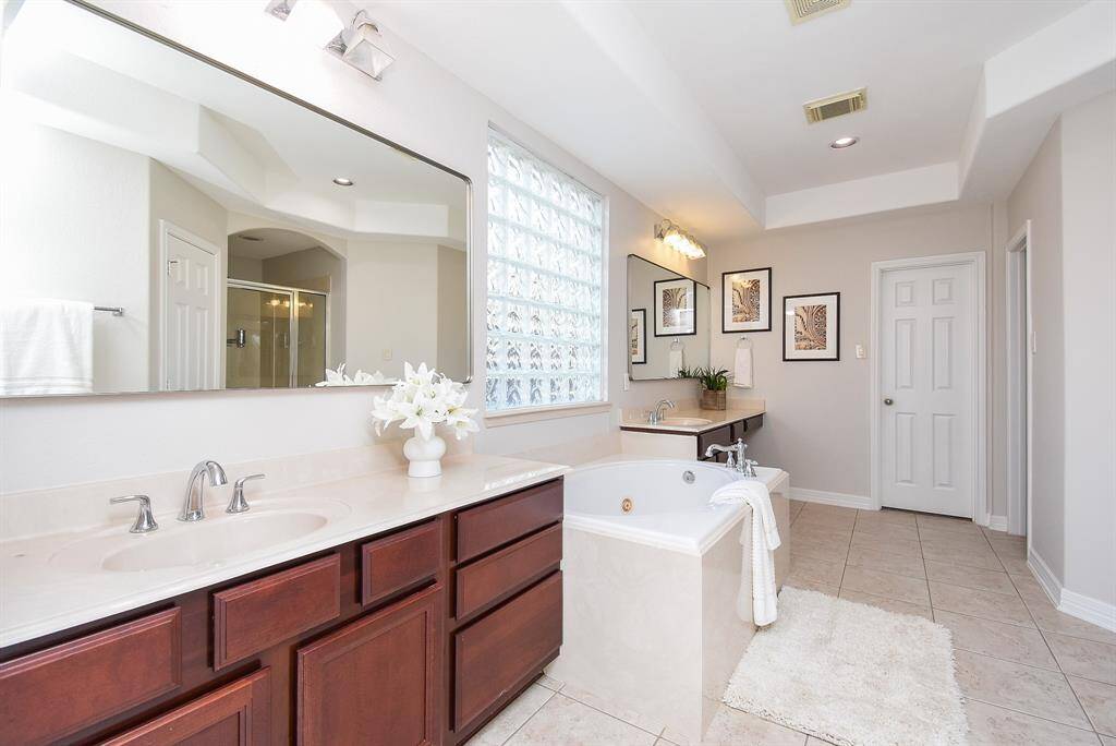 The en suite bath combines function and elegance, featuring dual vanities with dark cabinetry, each topped with wide mirrors. A soaking tub is the centerpiece, perfect for relaxing evenings.