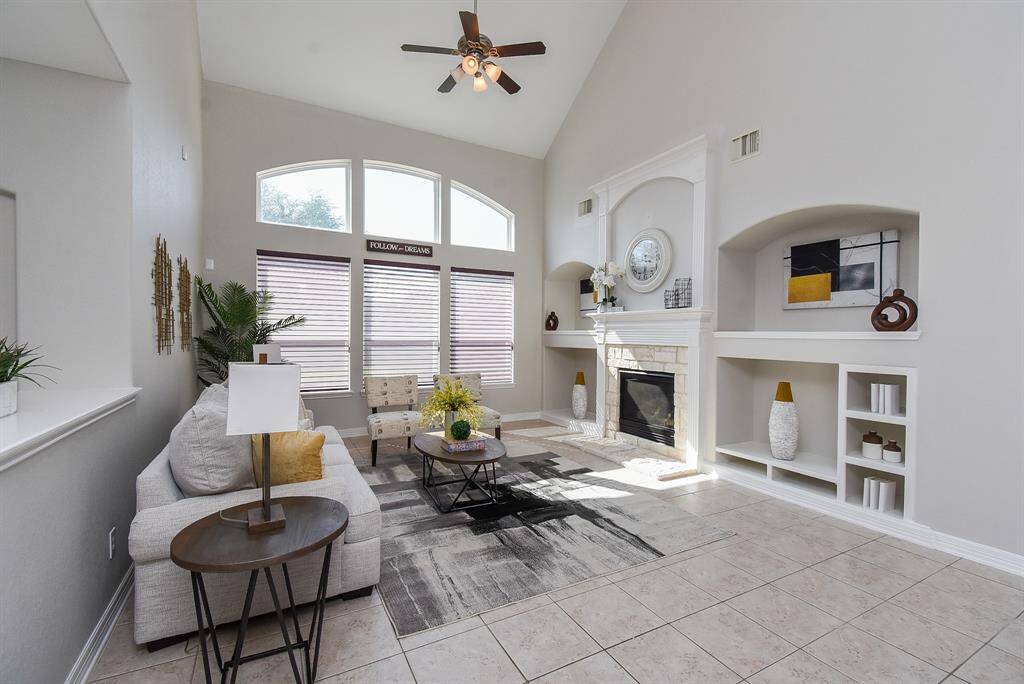 The living room features soaring ceilings, a central fireplace framed by tasteful wall niches, and an array of windows that invite natural light. The second-floor walkway above offers a dramatic overlook and visual connection to the entry below.