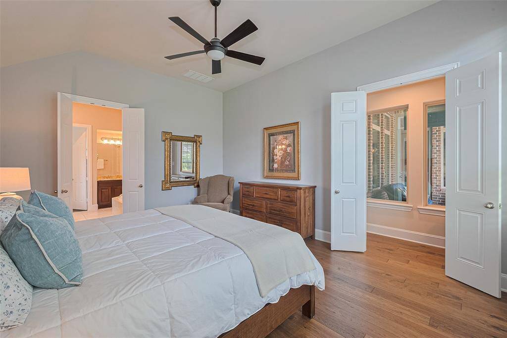 The primary bedroom features the same warm wood floors, a soothing neutral palette, and an updated ceiling fan. For added convenience, a wall mount for a TV is discreetly hidden behind the artwork, should you prefer to add one