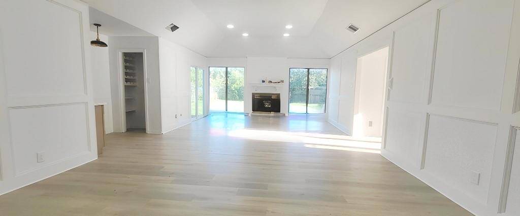 This spacious, bright living room features light wood flooring, high ceilings, and large sliding glass doors that open to a lush backyard. It includes a modern fireplace and elegant wall paneling, creating a perfect blend of style and comfort.