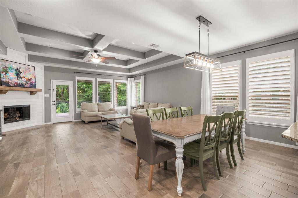 The inviting dining area is perfect for family meals or a quiet morning coffee. It features elegant wood-look tile flooring, a decorative chandelier, and two sun-filled windows with plantation shutters that create a bright, cheerful atmosphere.