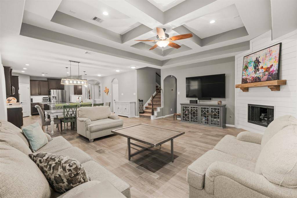 Family room features include recessed lighting, dramatic coffered tray ceiling, large wall for bookshelves or your electronics, and lighted ceiling fan. The staircase to upstairs is located in the center of the home for family convenience. This home offers a stunning view of its elegant design, with sightlines extending toward the kitchen and foyer. The open-concept floor plan effortlessly combines family living with the ideal space for entertaining, making it a perfect blend of style and functionality.