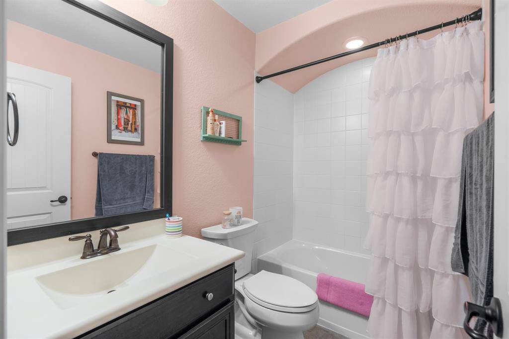 The second full en suite bathroom for Bedroom 2 features tile flooring, a solid surface countertop with integrated sink, toilet, framed mirror, and a tiled shower/tub combo with barrel ceiling.
