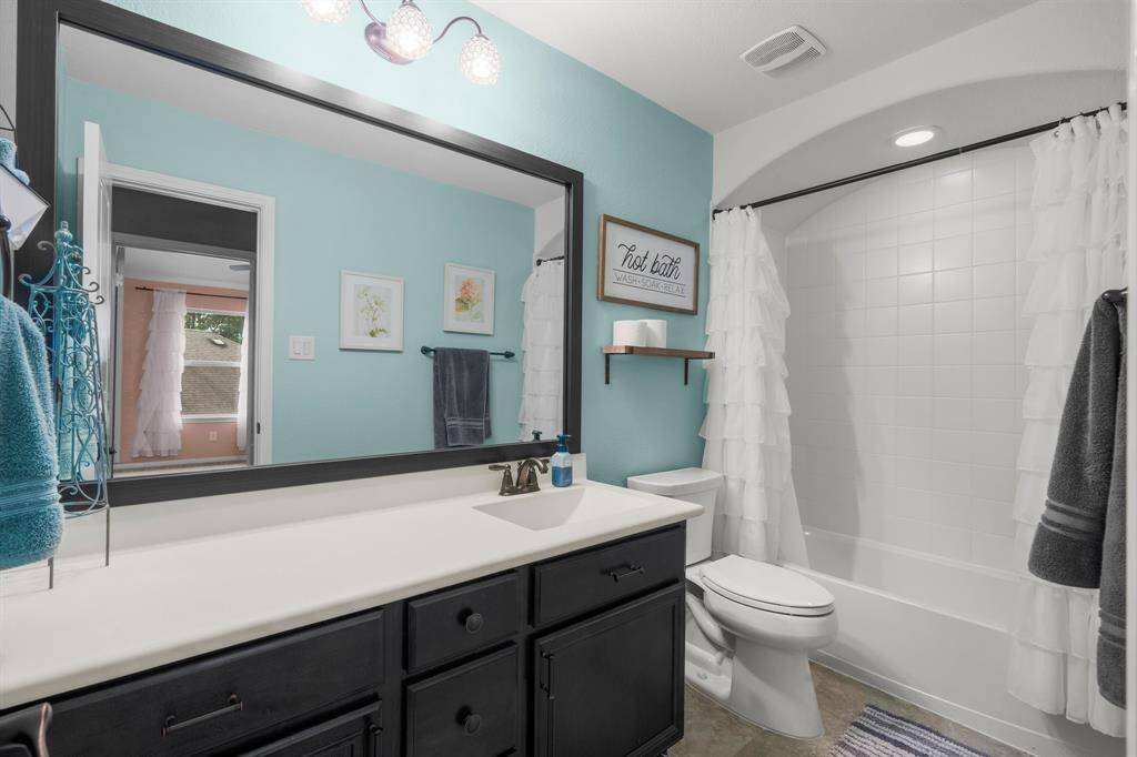 This full bath services the third and fourth secondary bedrooms. It features tile flooring, extended solid surface countertop with integrated sink, toilet, framed mirror, hallway linen closet, and tiled shower/tub combo with barrel ceiling.