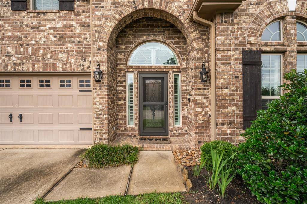 Luxury starts at the gorgeous covered front porch, featuring a stately wood, glass, and iron front door surrounded by two sidelights and an arched transom above. Thoughtful architectural features include detailed brick work around the windows and garage door, brick flooring on the porch, and wood shutters. Inside, this custom home is packed with high-end details and upgrades at every turn, offering a perfect blend of elegance and comfort.