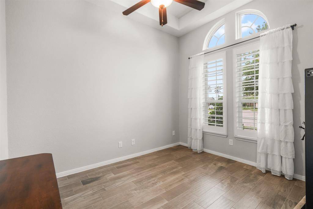 This executive office is a true standout with its high tray ceiling, filled with natural light from two large windows with overhead half-lunette window transoms. The study features elegant wood-look tile plank flooring, plantation shutters, and a lighted ceiling fan. French doors offer both sound control and privacy, while still allowing visibility into the main living areas of the home.