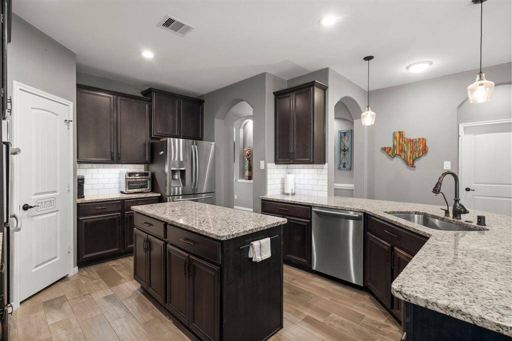 The stunning gourmet kitchen is the centerpiece of this exceptional home, featuring a spacious island with added storage and a peninsula with breakfast bar seating. Granite countertops, wood-look tile flooring, under-cabinet lighting, and a classic subway tile backsplash elevate both style and function. The walk-in pantry offers generous storage for appliances and culinary essentials.