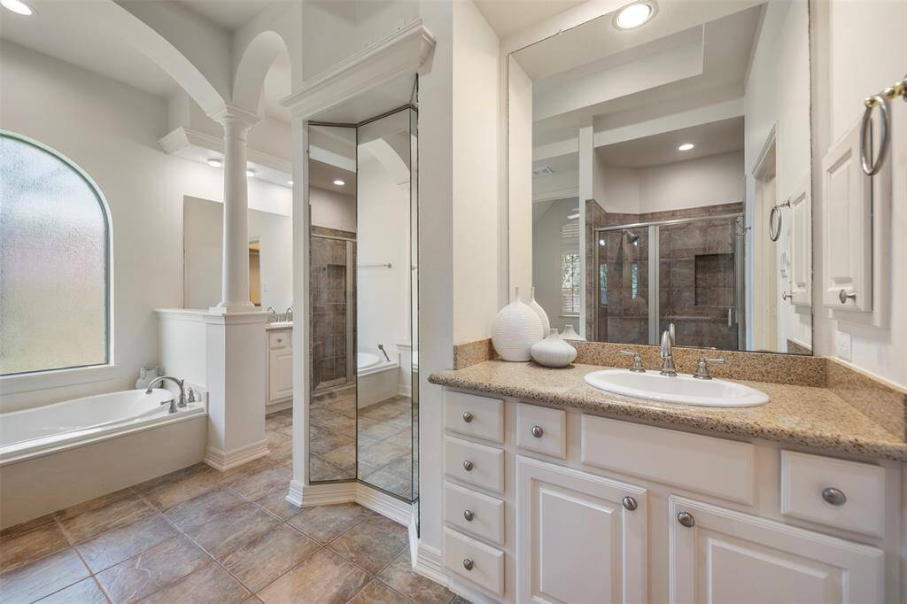 The primary bath is thoughtfully designed with stately pillars, a built-in three-way mirror, and dual granite vanities with his-and-her sinks, creating a luxurious and functional retreat.