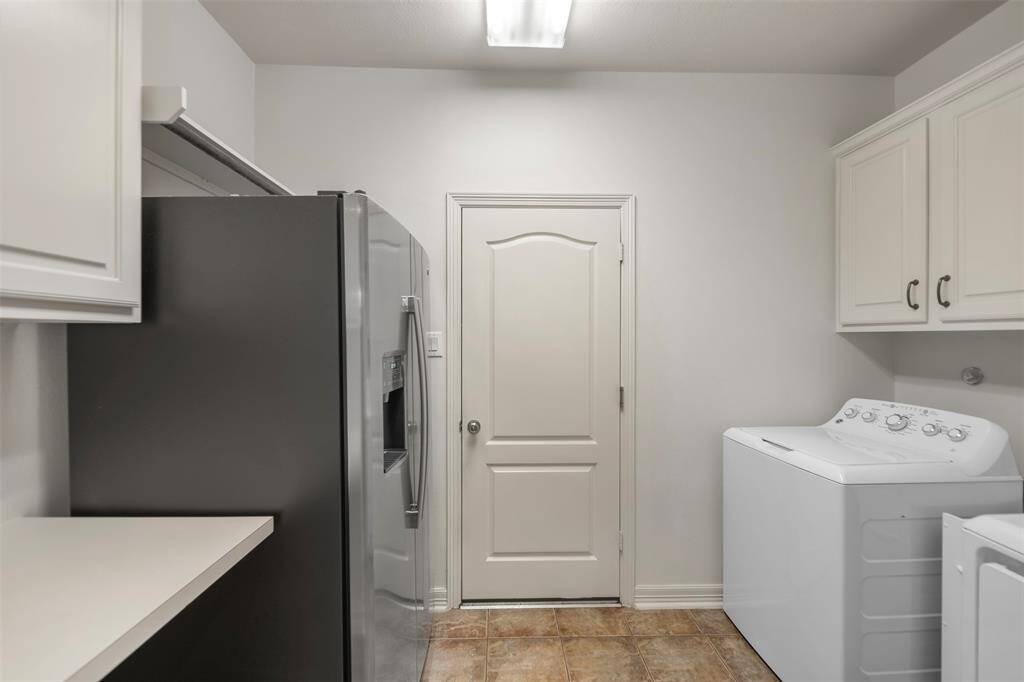 The laundry room features a washer and dryer, along with an additional stainless steel fridge for extra storage. A spacious counter provides a convenient folding area, while a door leads directly to the garage for easy access.