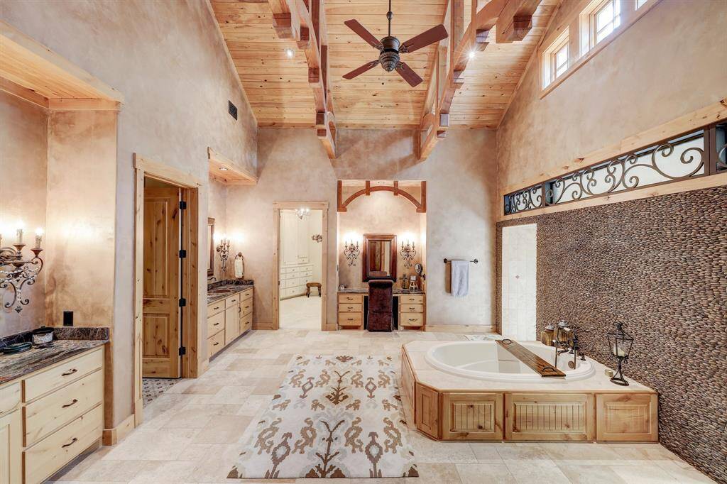 The primary bathroom includes dual sinks, a vanity area, soaking tub, stunning rock wall, and dual shower head walk in shower.