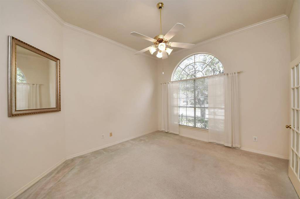 This room features a high ceiling with a central ceiling fan, a large arched window allowing plenty of natural light, neutral walls, and a carpeted floor, creating a bright and inviting space.