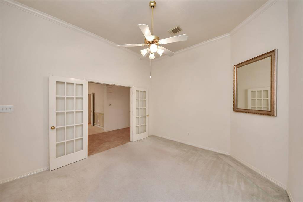 This room features neutral walls, carpeted flooring, and a ceiling fan. It includes French doors that lead to an adjacent space, adding charm and versatility. A large wall mirror enhances the sense of space.