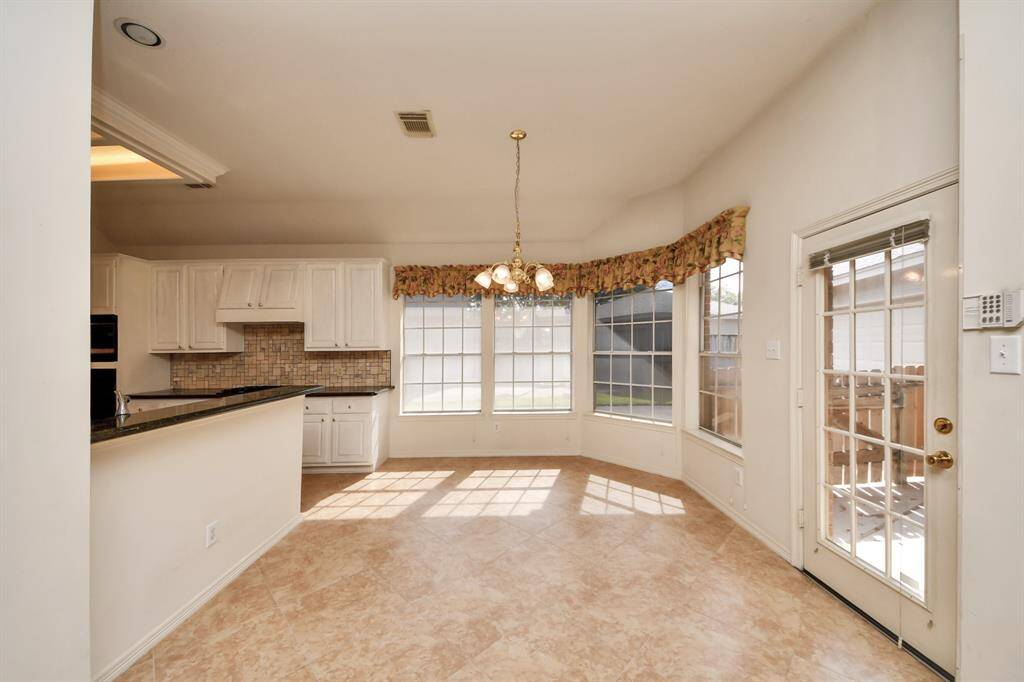 Bright kitchen and breakfast area with large windows, tile flooring, and a view of the backyard. Features white cabinetry, a breakfast bar with granite countertops, and French doors for outdoor access.