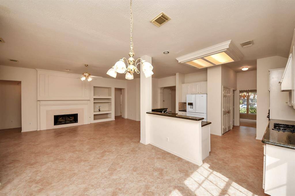 This photo showcases a spacious open-plan living area with tiled flooring and a fireplace. The room features a bright kitchen with white cabinetry and black countertops, adjacent to a dining area with elegant lighting. Large windows allow natural light to fill the space.